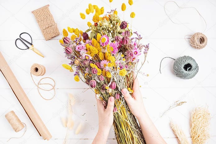 Woman composing bouquet of dry flowers and herbs, trendy interior decoration, artisan florist shop idea. Top view, flat lay